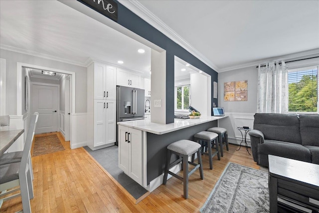 200 Merrick Rd Unit R, Amityville, NY 11701 - kitchen with a baseboard radiator, high quality fridge, a breakfast bar, white cabinetry, and ornamental molding