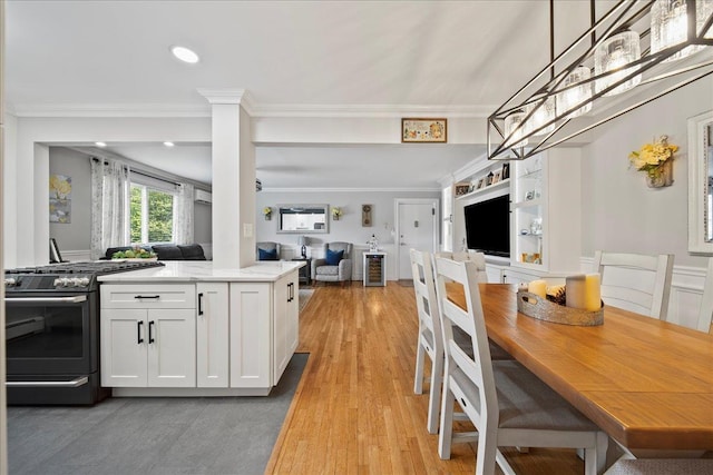 200 Merrick Rd Unit R, Amityville, NY 11701 - kitchen with gas range oven, open floor plan, white cabinetry, ornamental molding, and hanging light fixtures