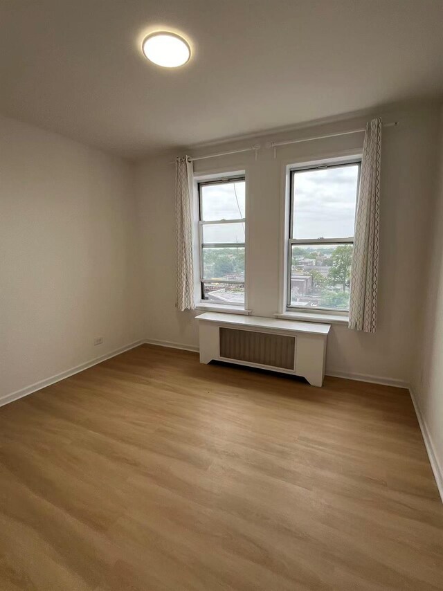 3591 161st St Unit 6L, Flushing, NY 11358 - spare room with radiator, plenty of natural light, light wood-style floors, and baseboards