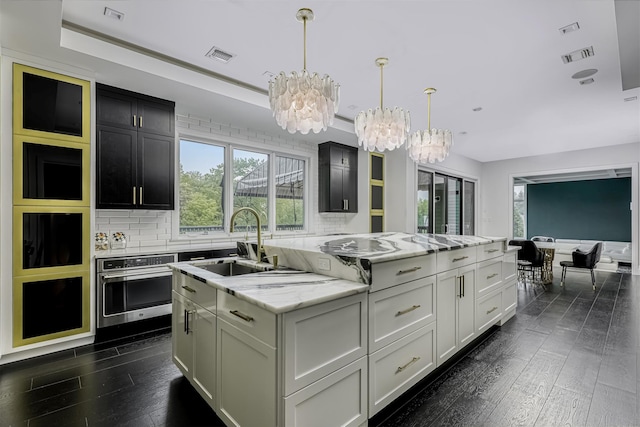 kitchen with a chandelier, a center island with sink, dark wood-style floors, and plenty of natural light