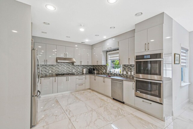 345 Washington Ave, Cedarhurst, NY 11516 - kitchen featuring appliances with stainless steel finishes, modern cabinets, a sink, light marble finish floors, and backsplash