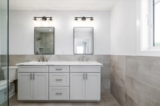 12 Pershing Pl, Island Park, NY 11558 - bathroom with double vanity, a tile shower, tile walls, a wainscoted wall, and tile patterned floors