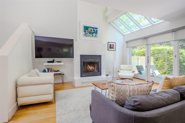 10 Head Of Pond Rd Unit 8, Water Mill, NY 11976 - living area with a skylight, a lit fireplace, light wood-style flooring, a high ceiling, and baseboards