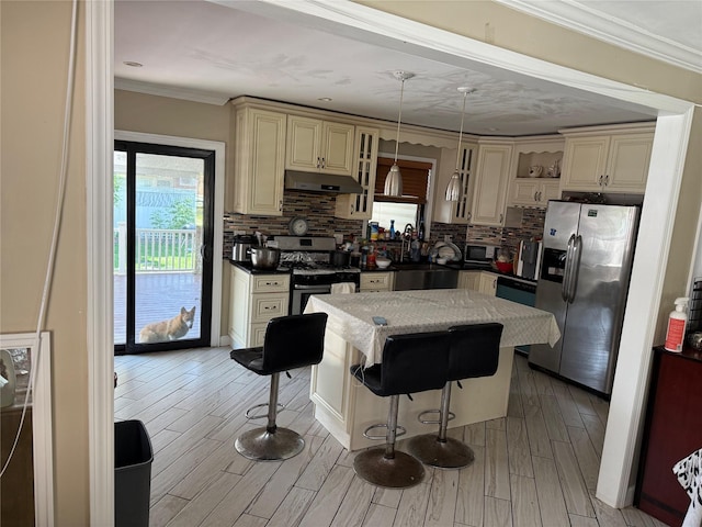 7308 187th St, Fresh Meadows, NY 11366 - kitchen featuring appliances with stainless steel finishes, cream cabinetry, under cabinet range hood, a kitchen island, and tasteful backsplash