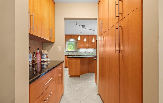 34 Oak Meadow Rd, Commack, NY 11725 - kitchen featuring decorative backsplash, light tile patterned floors, dark stone counters, hanging light fixtures, and brown cabinetry
