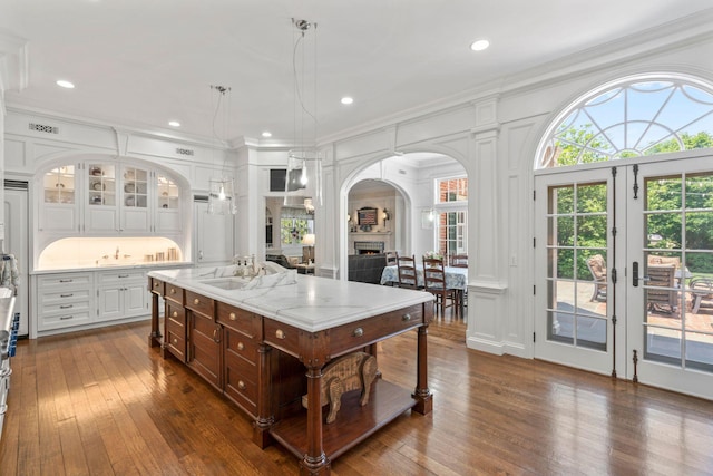 7 Fox Meadow Ln, Lloyd Harbor, NY 11743 - kitchen featuring arched walkways, dark wood-style flooring, glass insert cabinets, white cabinets, and decorative light fixtures
