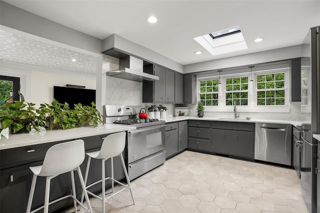 71 Baraud Rd S, Scarsdale, NY 10583 - kitchen featuring appliances with stainless steel finishes, wall chimney exhaust hood, a skylight, gray cabinets, and backsplash