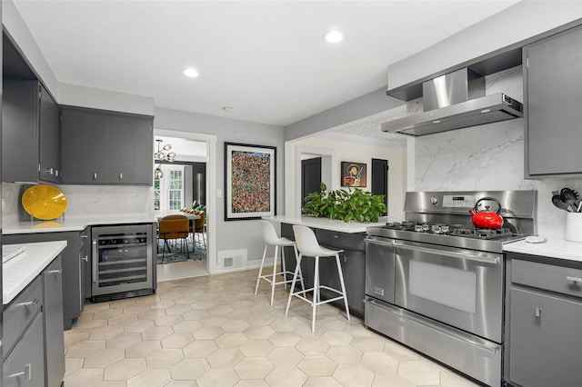 71 Baraud Rd S, Scarsdale, NY 10583 - kitchen with stainless steel range with gas cooktop, wall chimney range hood, wine cooler, gray cabinetry, and backsplash