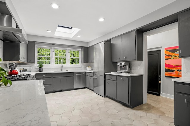 71 Baraud Rd S, Scarsdale, NY 10583 - kitchen featuring a skylight, wall chimney exhaust hood, stainless steel appliances, decorative backsplash, and gray cabinetry