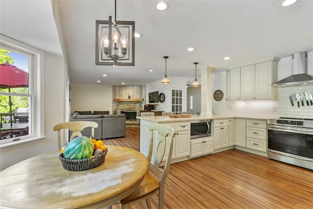 41 Indian Hill Rd, Brewster, NY 10509 - kitchen with wall chimney range hood, stainless steel appliances, a peninsula, tasteful backsplash, and light wood finished floors