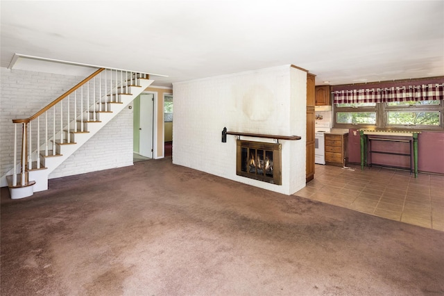94 E Way, Mount Kisco, NY 10549 - unfurnished living room featuring brick wall, stairway, a glass covered fireplace, healthy amount of natural light, and carpet floors