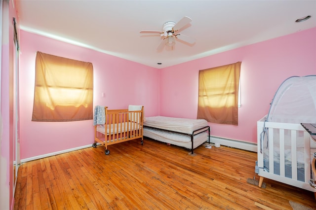 3929 Greentree Dr, Oceanside, NY 11572 - bedroom featuring a baseboard heating unit, hardwood / wood-style floors, ceiling fan, and baseboards