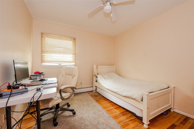 3929 Greentree Dr, Oceanside, NY 11572 - bedroom featuring a baseboard heating unit, an office area, wood finished floors, ceiling fan, and baseboards