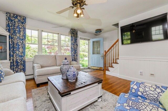 96 N Howells Point Rd, Bellport Village, NY 11713 - living room featuring a baseboard heating unit, ceiling fan, wood finished floors, stairs, and a wainscoted wall