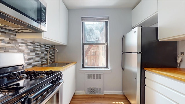 65-35 108th St Unit D7, Forest Hills, NY 11375 - kitchen with appliances with stainless steel finishes, radiator, a sink, decorative backsplash, and white cabinetry