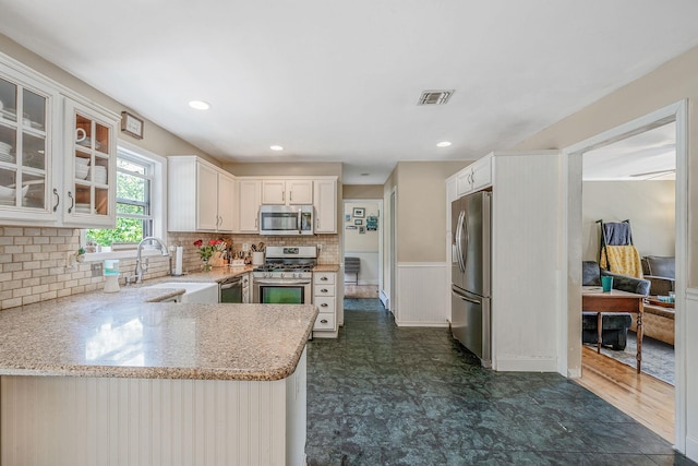 4 Ariel Ct, Rocky Point, NY 11778 - kitchen with appliances with stainless steel finishes, light stone countertops, white cabinets, glass insert cabinets, and decorative backsplash