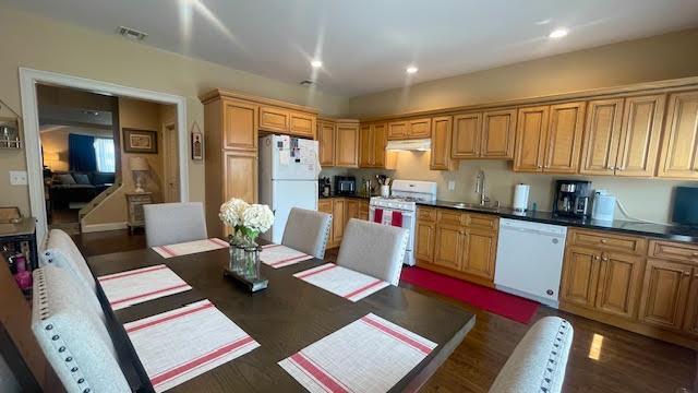 2568 Seminole Ave, Seaford, NY 11783 - kitchen with white appliances, dark countertops, under cabinet range hood, recessed lighting, and dark wood finished floors