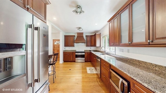 1002 Kitchawan Rd, Ossining, NY 10562 - kitchen featuring stainless steel appliances, premium range hood, light wood-type flooring, light stone countertops, and glass insert cabinets