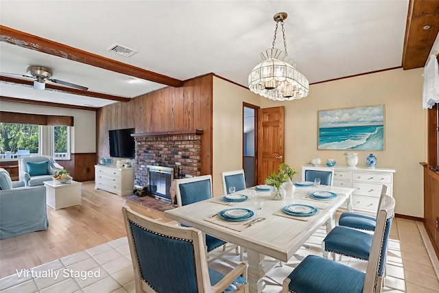 109 Dogwood Ln, Port Jefferson, NY 11777 - dining space featuring light tile patterned floors, beam ceiling, a chandelier, a brick fireplace, and wooden walls