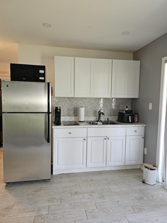 943 Macarthur St, Bohemia, NY 11716 - kitchen featuring freestanding refrigerator, black microwave, white cabinetry, decorative backsplash, and light wood finished floors