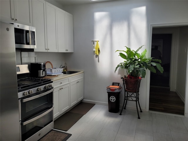 3039 Fulton St, Brooklyn, NY 11208 - kitchen featuring stainless steel appliances, decorative backsplash, baseboards, a sink, and white cabinets
