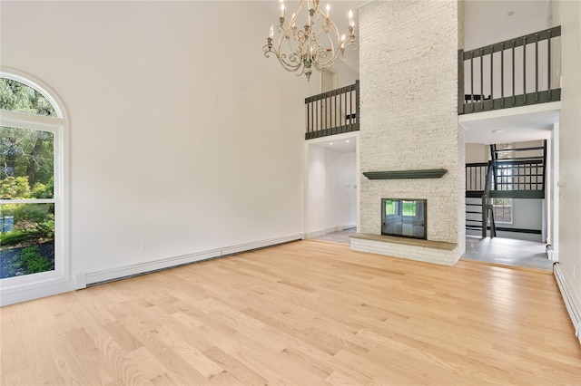 17 Royal Ct, Warwick, NY 10990 - unfurnished living room featuring baseboard heating, wood finished floors, a towering ceiling, a chandelier, and a large fireplace