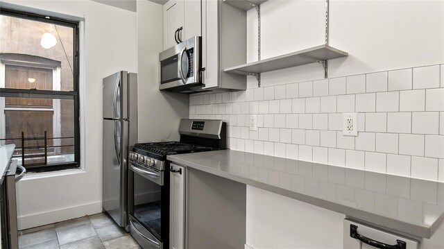 1037 College Ave, Bronx, NY 10456 - kitchen featuring appliances with stainless steel finishes, backsplash, baseboards, and white cabinets