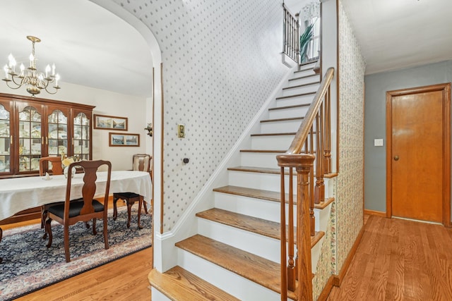 54 Ogden Ave, East Williston, NY 11596 - staircase featuring wood finished floors, wallpapered walls, arched walkways, a chandelier, and baseboards