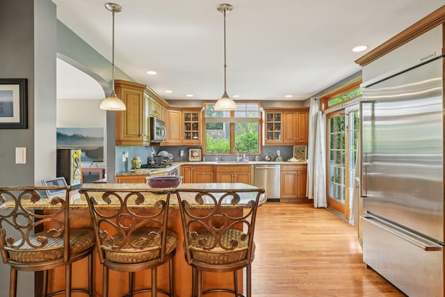 54 Ogden Ave, East Williston, NY 11596 - kitchen featuring stainless steel appliances, light wood-type flooring, a breakfast bar area, brown cabinets, and glass insert cabinets