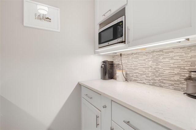 210 E 63rd St Unit 10E, New York Manhattan, NY 10065 - kitchen with stainless steel microwave, backsplash, white cabinetry, and light stone counters