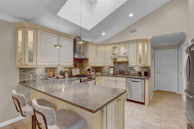 738 Craft Ave, Franklin Square, NY 11010 - kitchen featuring appliances with stainless steel finishes, cream cabinets, wall chimney exhaust hood, a peninsula, and vaulted ceiling