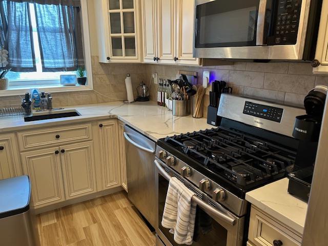 504 Merrick Rd Unit 4E, Lynbrook, NY 11563 - kitchen featuring stainless steel appliances, cream cabinetry, glass insert cabinets, tasteful backsplash, and light wood-style flooring