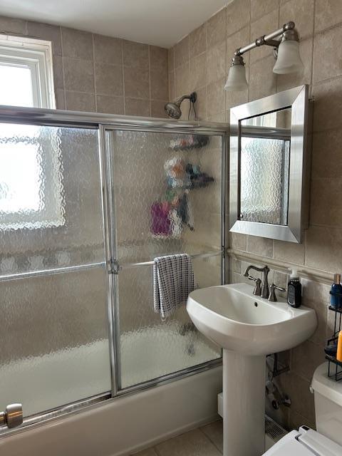 504 Merrick Rd Unit 4E, Lynbrook, NY 11563 - bathroom with tile walls, shower / bath combination with glass door, tile patterned flooring, and backsplash