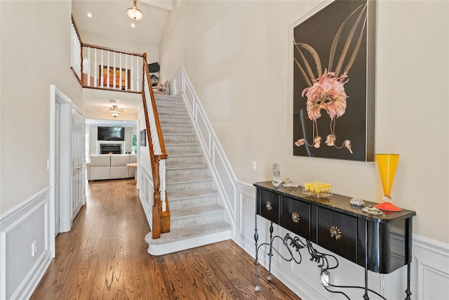 81 Hidden Ridge Dr, Syosset, NY 11791 - stairs with a decorative wall, wood finished floors, a wainscoted wall, and a warm lit fireplace