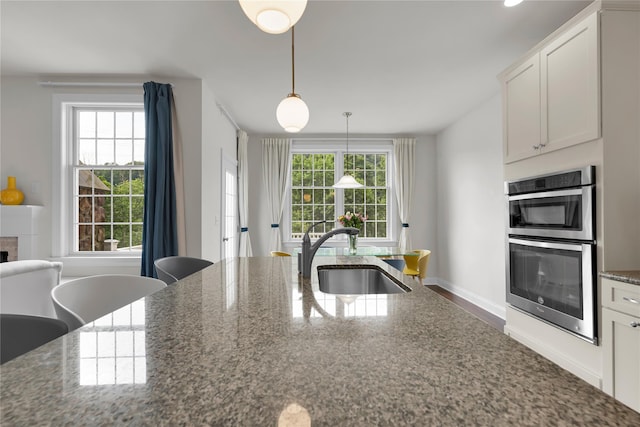 20 Dennis Ln, Pleasantville, NY 10570 - kitchen featuring stainless steel double oven, decorative light fixtures, white cabinetry, dark stone countertops, and a tiled fireplace