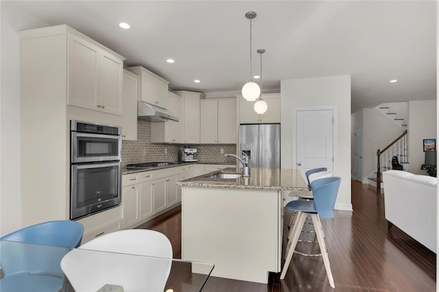 20 Dennis Ln, Pleasantville, NY 10570 - kitchen with stainless steel appliances, under cabinet range hood, backsplash, a center island with sink, and light stone counters