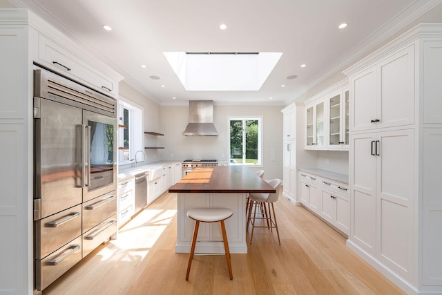 1750 Mount Beulah Ave, Southold, NY 11971 - kitchen featuring high end appliances, wall chimney range hood, light wood-style flooring, a skylight, and wooden counters