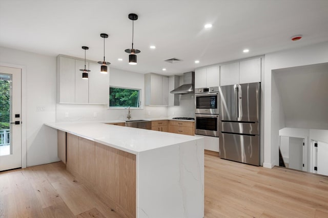 8 Junard Dr, Roslyn, NY 11576 - kitchen featuring stainless steel appliances, wall chimney exhaust hood, a peninsula, light wood-style flooring, and hanging light fixtures