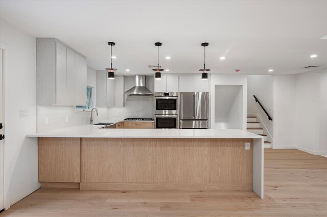8 Junard Dr, Roslyn, NY 11576 - kitchen featuring appliances with stainless steel finishes, wall chimney range hood, a peninsula, light countertops, and recessed lighting