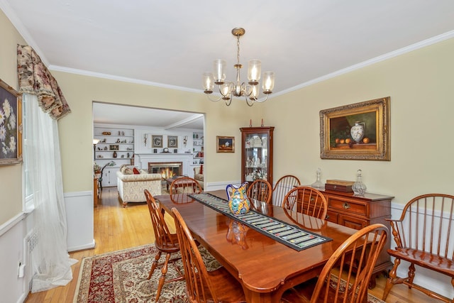 2 The Spout, Smithtown, NY 11787 - dining room with ornamental molding, a lit fireplace, a chandelier, and light wood finished floors