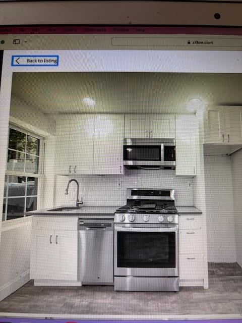 135 Saint Marks Ave, Brooklyn, NY 11217 - kitchen with stainless steel appliances, a sink, dark wood-type flooring, tasteful backsplash, and white cabinets