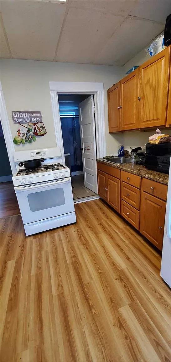 77 Carroll St, Poughkeepsie, NY 12601 - kitchen with white gas range, brown cabinetry, light wood finished floors, dark countertops, and a drop ceiling