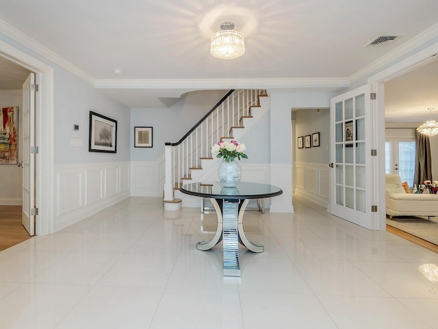 70 Scudders Ln, Roslyn Harbor, NY 11576 - tiled foyer entrance with a chandelier, stairway, ornamental molding, a decorative wall, and wainscoting