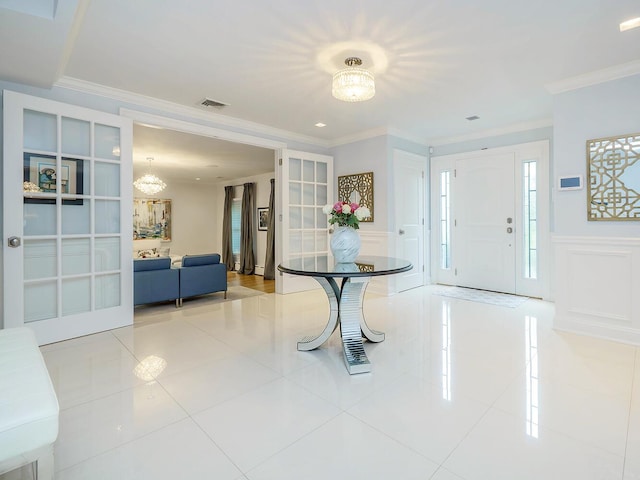 70 Scudders Ln, Roslyn Harbor, NY 11576 - foyer entrance featuring a chandelier, a decorative wall, ornamental molding, tile patterned floors, and wainscoting