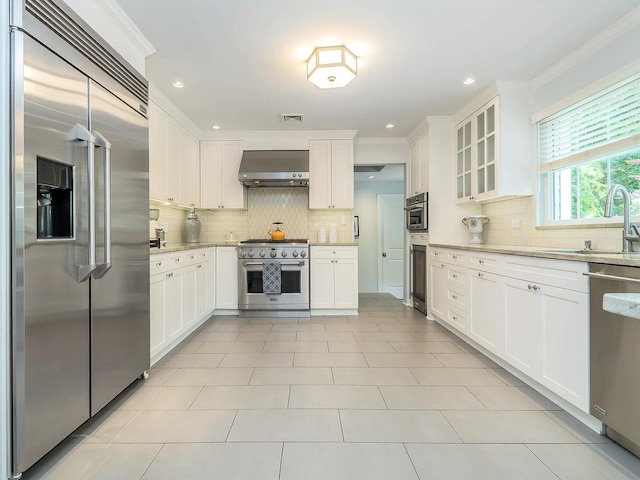 70 Scudders Ln, Roslyn Harbor, NY 11576 - kitchen featuring premium appliances, wall chimney range hood, decorative backsplash, white cabinetry, and ornamental molding