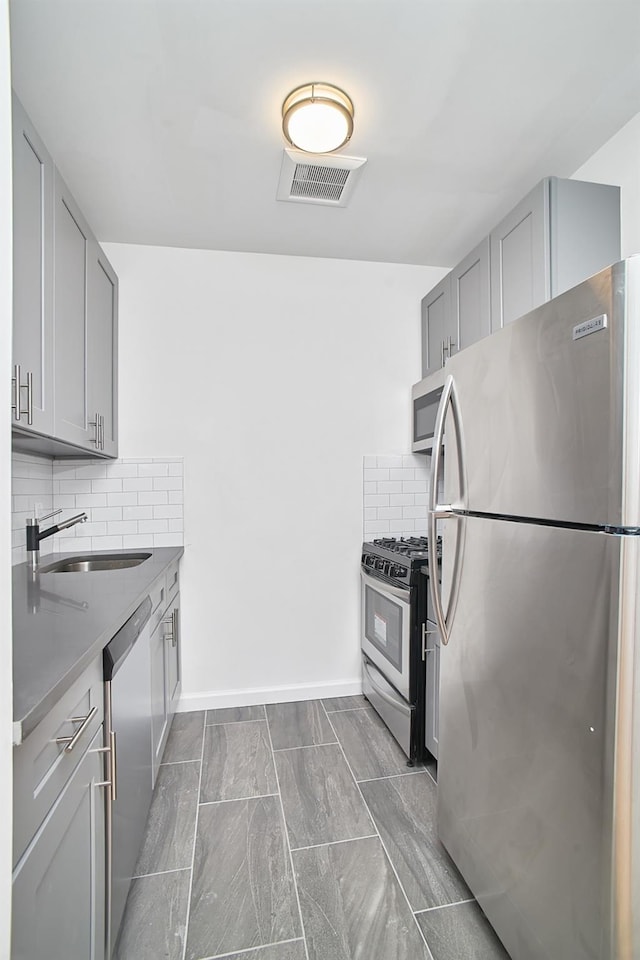 1069 Grant Ave, Bronx, NY 10456 - kitchen with stainless steel appliances, a sink, gray cabinetry, decorative backsplash, and baseboards