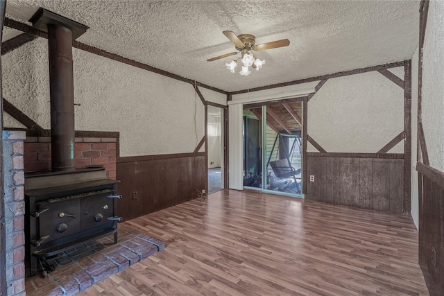 168 Gibbs Rd, Central Islip, NY 11722 - unfurnished living room with a textured wall, a textured ceiling, a wood stove, wood finished floors, and ceiling fan