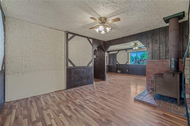 168 Gibbs Rd, Central Islip, NY 11722 - spare room with ceiling fan, a wood stove, a textured ceiling, wood finished floors, and wooden walls
