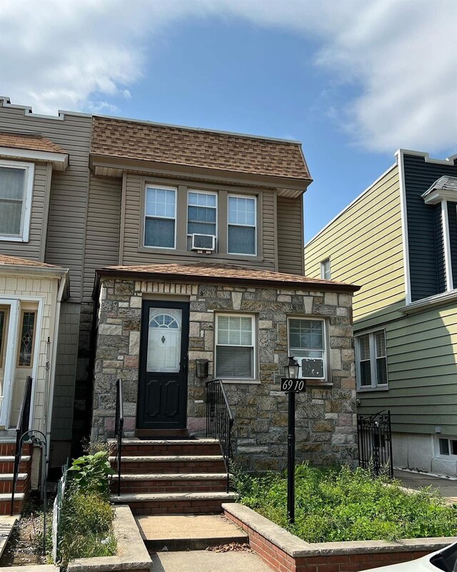 6910 68th St, Glendale, NY 11385 - view of front of property featuring stone siding, cooling unit, a shingled roof, and entry steps