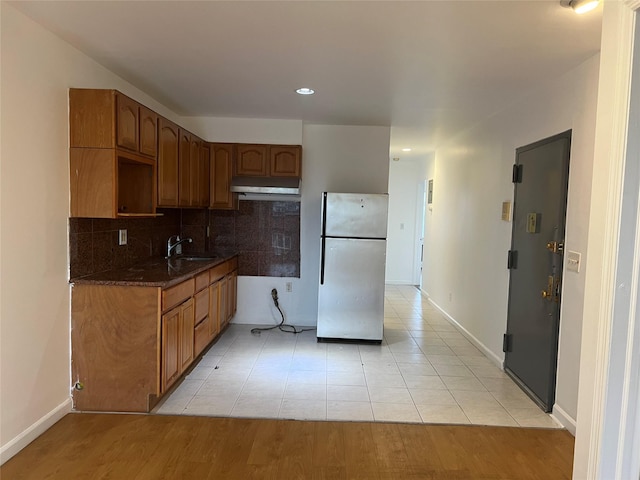55-05 98th St, Corona, NY 11368 - kitchen with freestanding refrigerator, under cabinet range hood, decorative backsplash, light tile patterned flooring, and brown cabinets